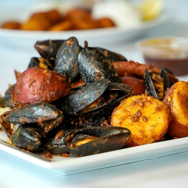 Boil Daddy's mussels and potatoes coated in a rich, dark sauce, served on a white plate.