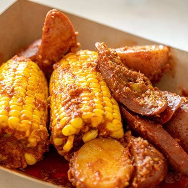 Boil Daddy's Cajun seafood boil with corn on the cob, potatoes, and sausage in a takeout container.